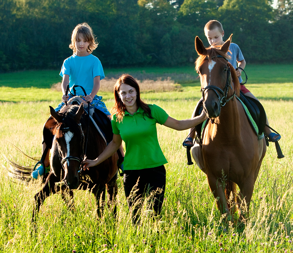 two kids riding horses being led by a woman